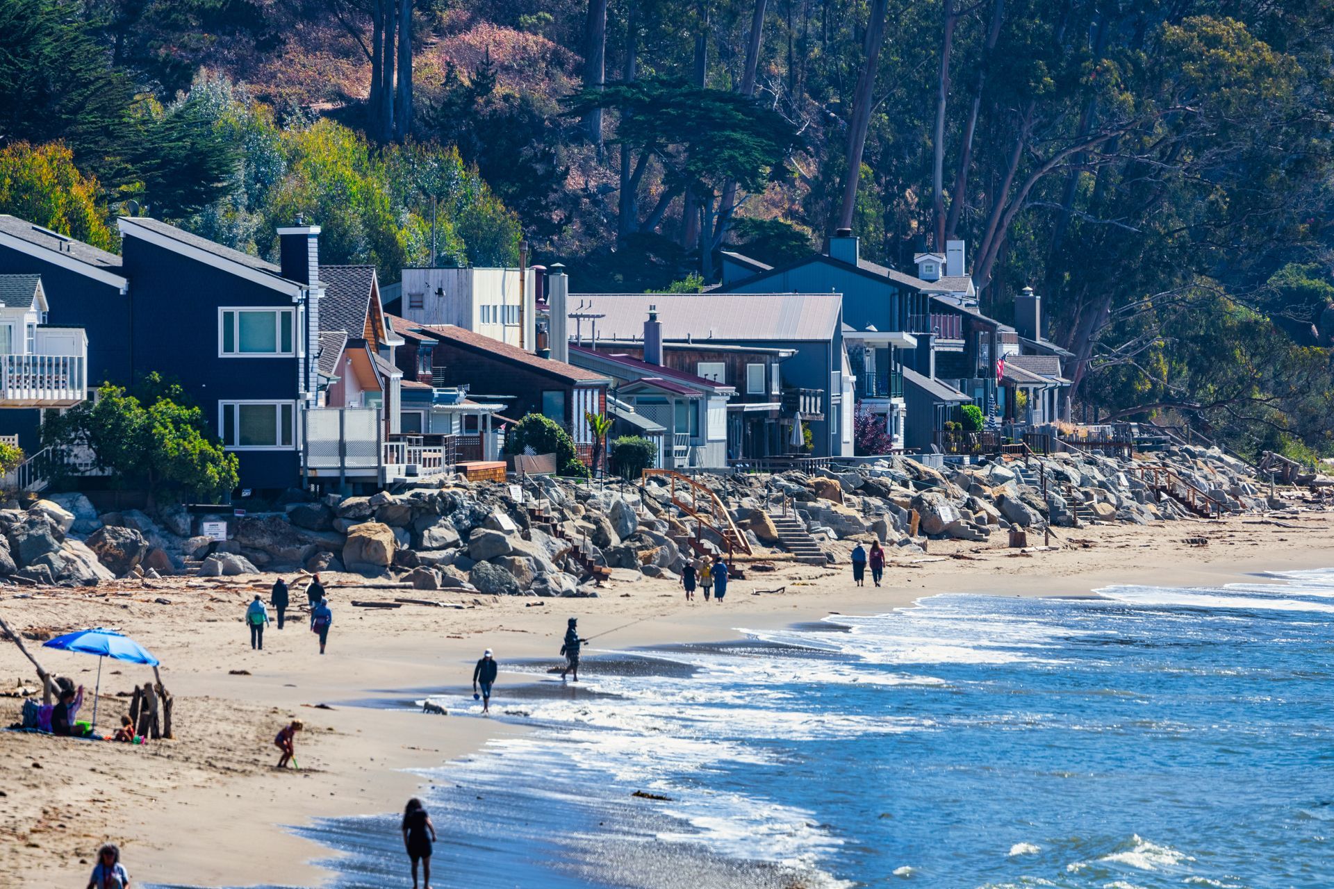 Beach with houses, people, and ocean. Blue houses line a sandy shore, people walk on the beach. Beach with houses, people, and ocean. Blue houses line a sandy shore, people walk on the beach.