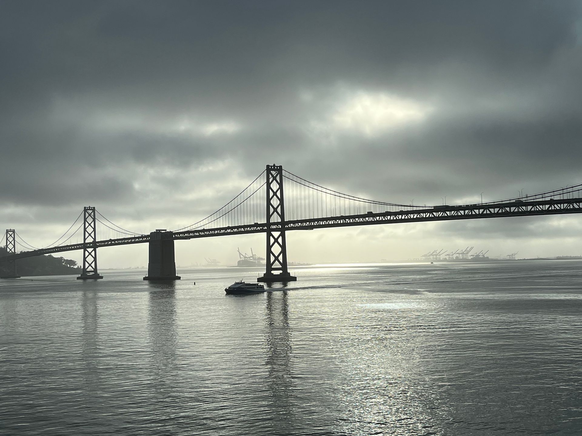 Bay Bridge under a cloudy sky, with dark water and a boat.