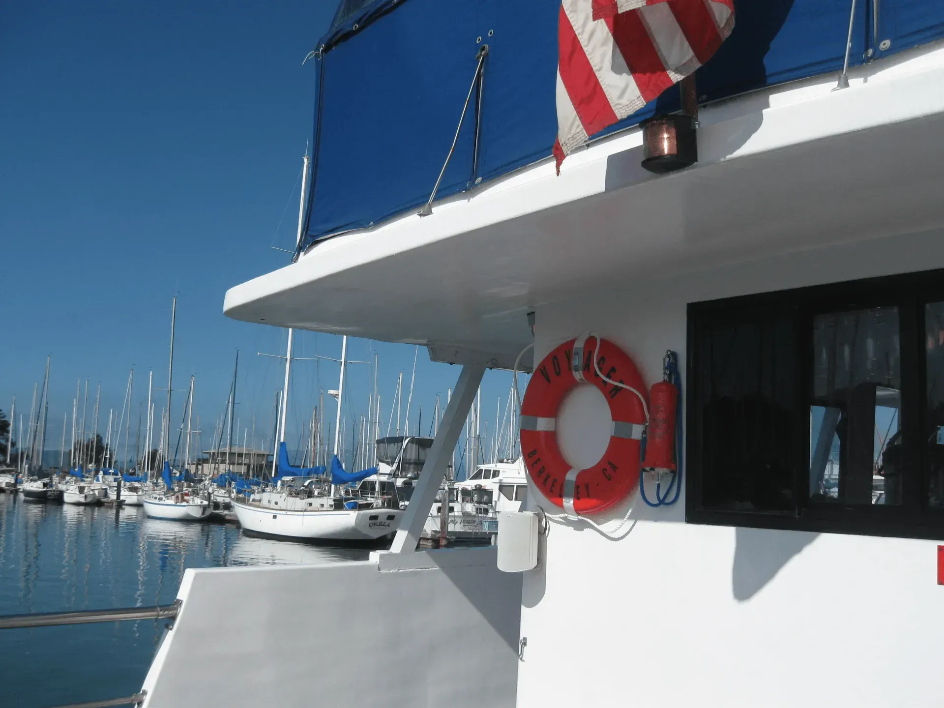 White boat with a life preserver and American flag, docked in a harbor with many sailboats.