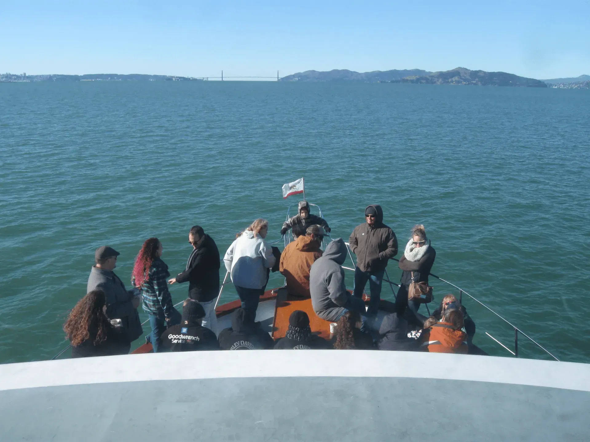 People on a boat looking at water, Golden Gate Bridge in the distance. Blue sky and ocean.