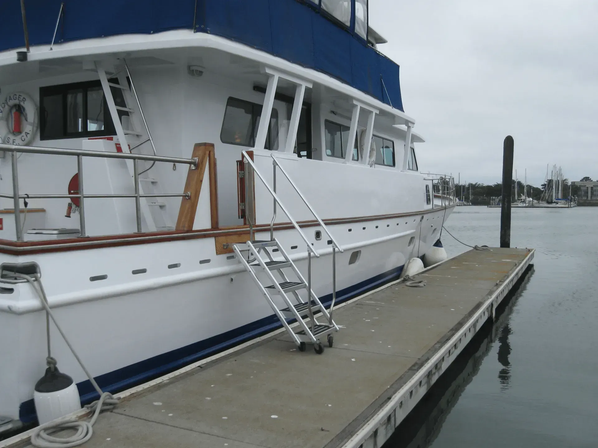 White and blue boat docked at a pier, with a rolling aluminum ladder.