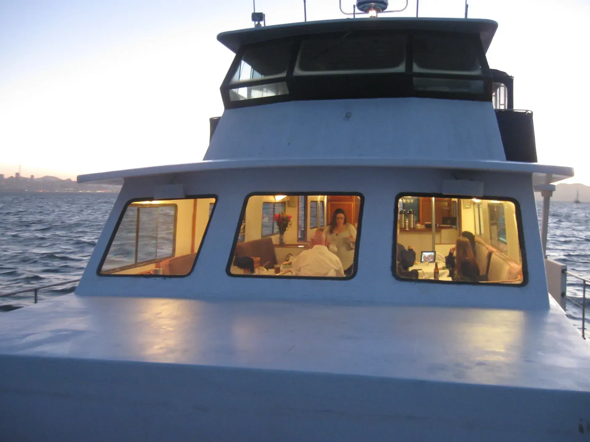 Boat cabin with lit windows, people inside, on water at dusk.