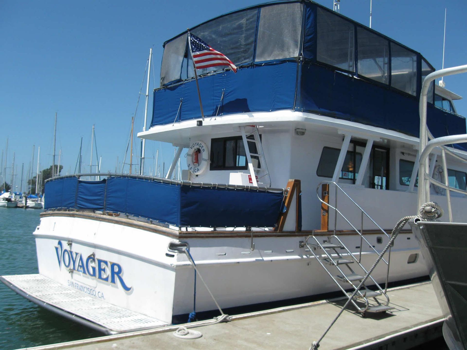 Golden Gate Bridge spans the blue water under a bright blue sky, viewed from a rocky shore.
