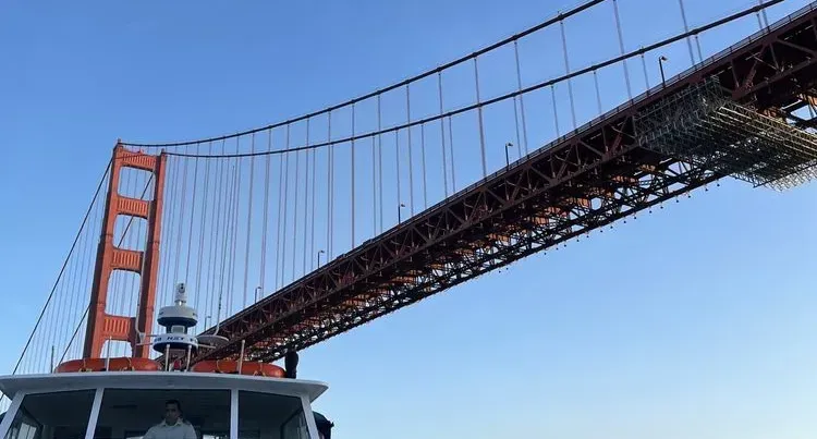 Boat under Golden Gate Bridge, looking up at red towers and cables against a blue sky.