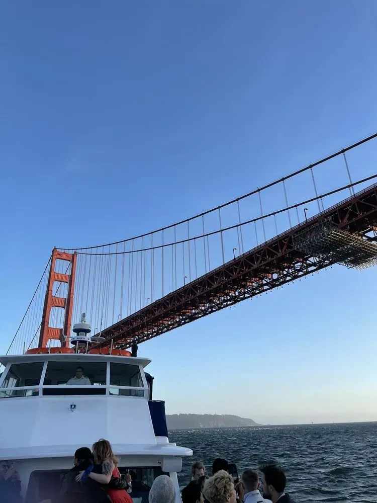 Boat under the Golden Gate Bridge in San Francisco. People on deck, blue sky, water.