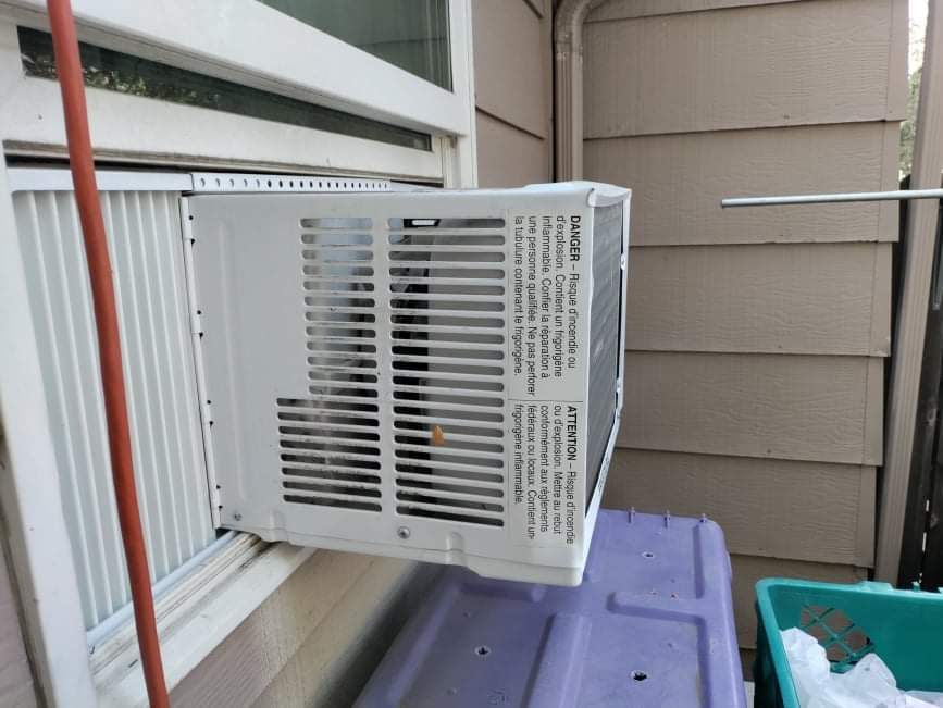 A window air conditioner is hanging from the side of a house