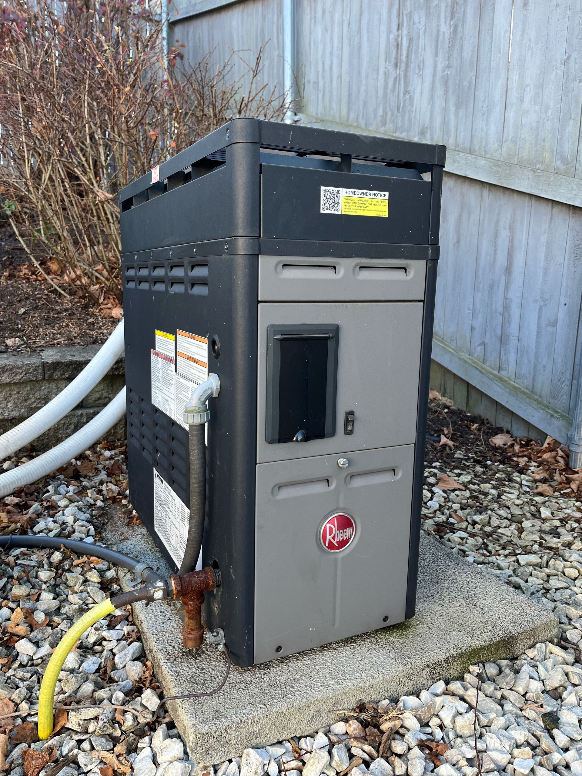 pool heater is sitting on top of a pile of gravel next to a fence.