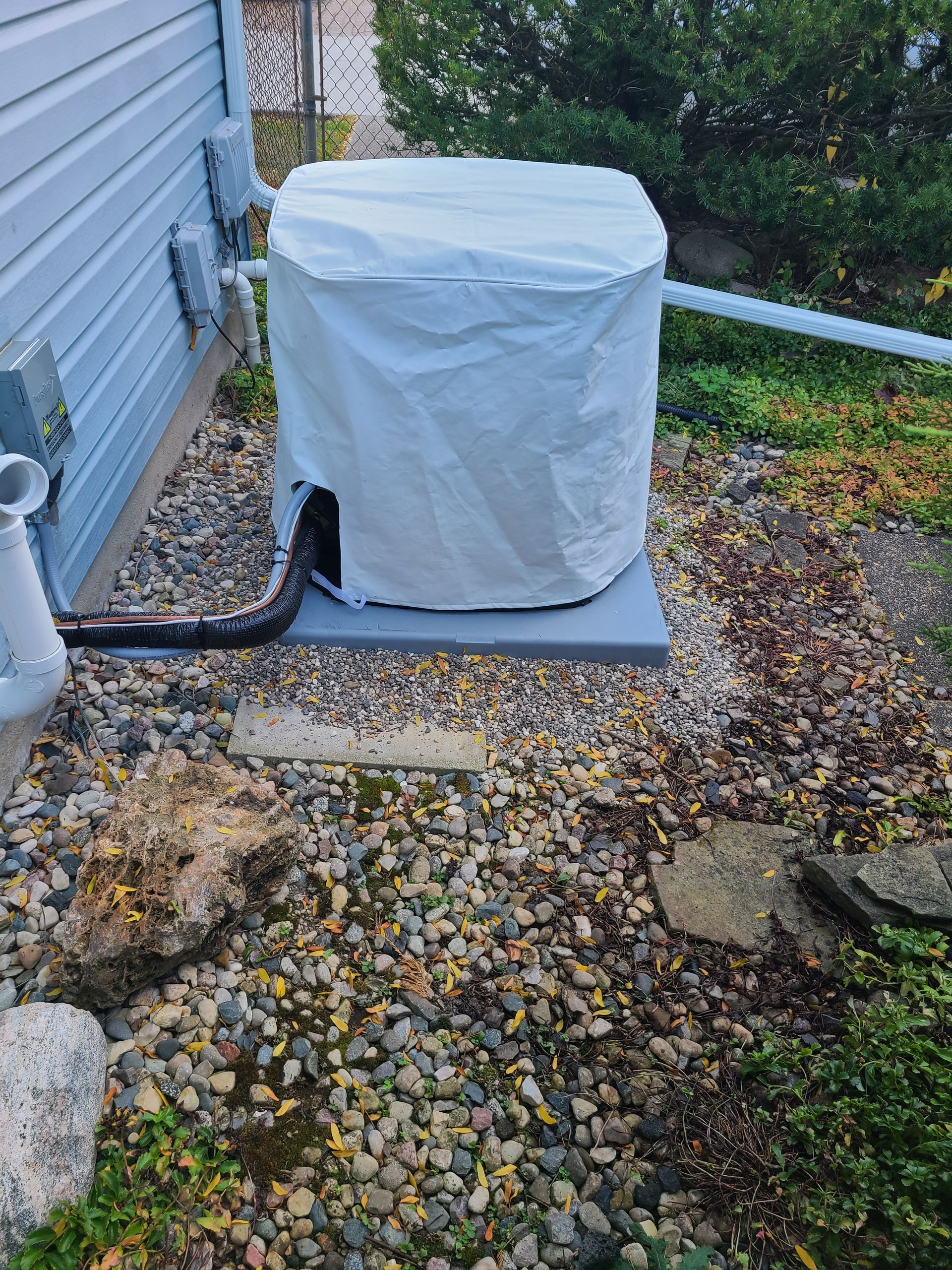 A white cover is covering an air conditioner outside of a house.