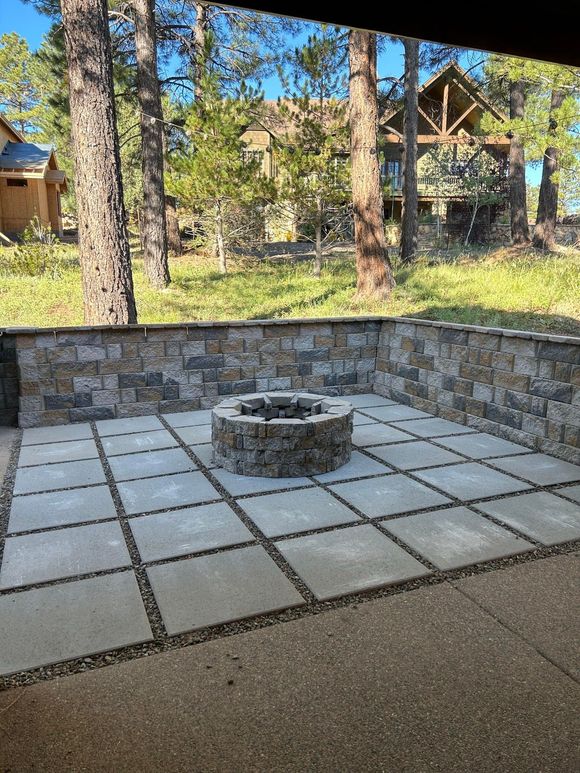 A patio with chairs and a fire pit in front of a house in the woods.