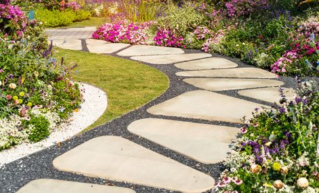 A stone walkway in a garden surrounded by flowers and grass.