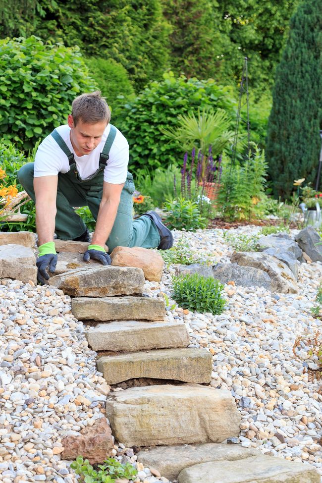 A man is laying stone steps in a garden.