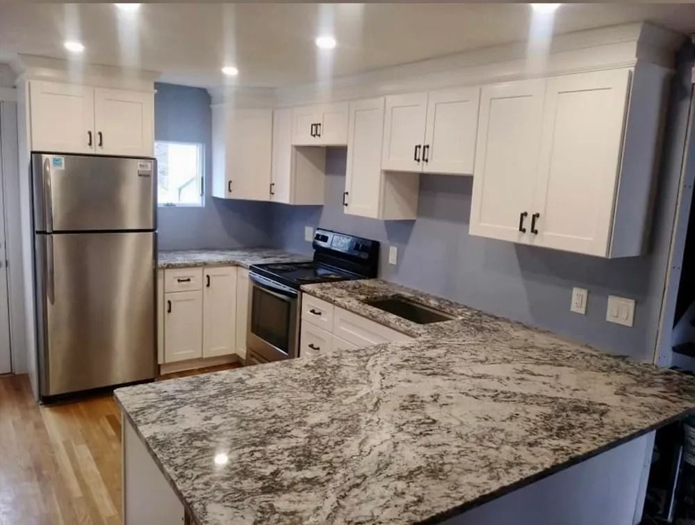 Bright modern kitchen with white cabinets, stainless fridge, gas stove, and granite island countertop