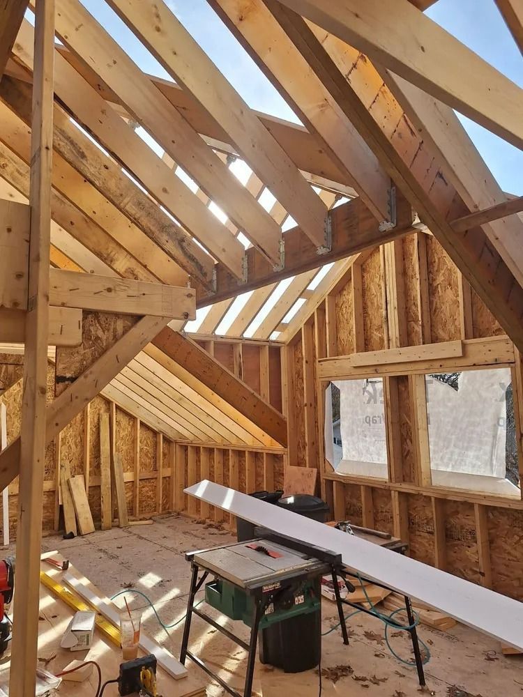 Unfinished attic with exposed wooden framing, a workbench, and daylight through roof and wall openings