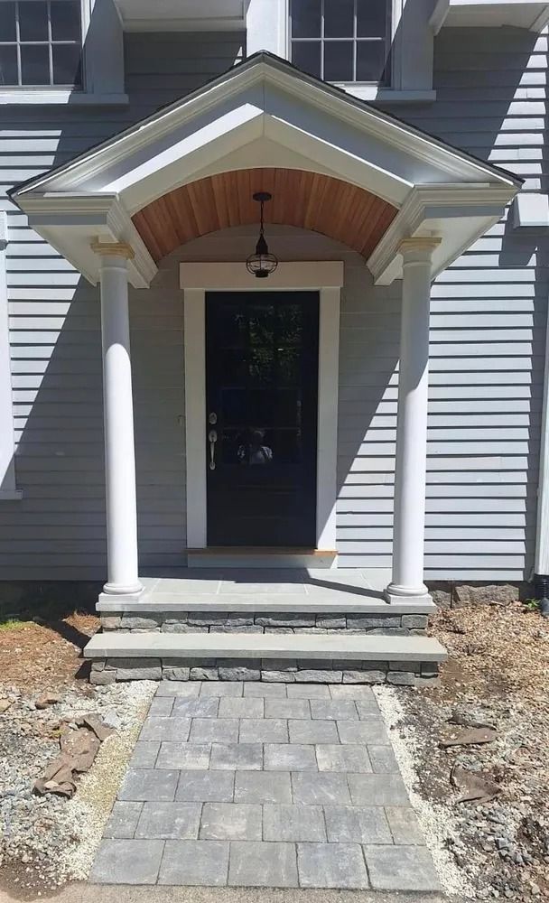 Front porch with white columns, dark entry door, and stone walkway leading to a gray house