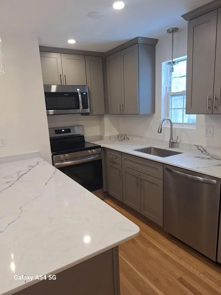 Modern kitchen with gray cabinets, white countertops, stainless appliances, and hardwood floors.
