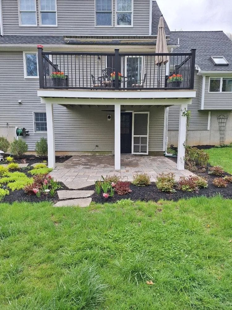 Backyard patio with covered deck, stairs, potted plants, and landscaped garden beds behind a house