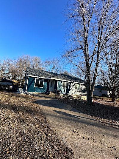 A blue house is sitting on the side of a dirt road next to a tree.