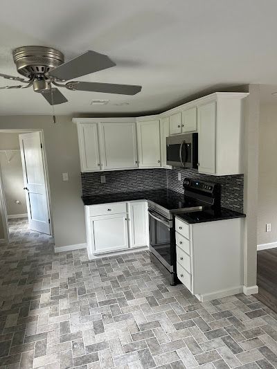 A kitchen with white cabinets , a stove , a microwave , and a ceiling fan.