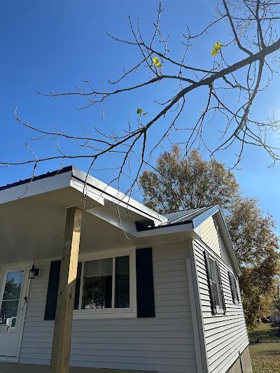 A small white house with a porch and a tree in the background.