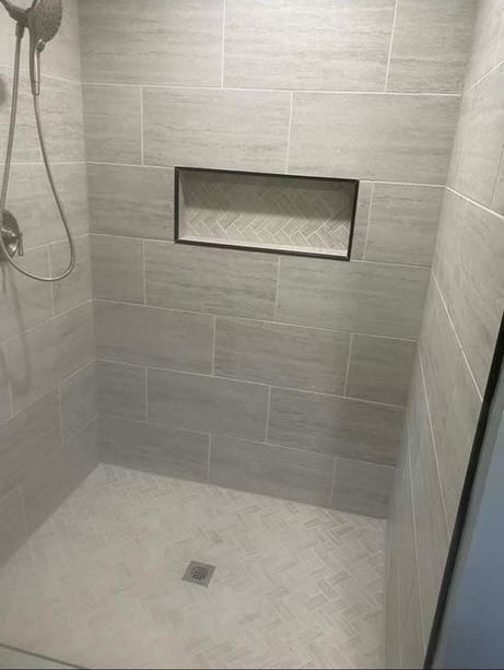 A walk in shower with a shower head and a shelf in the wall.
