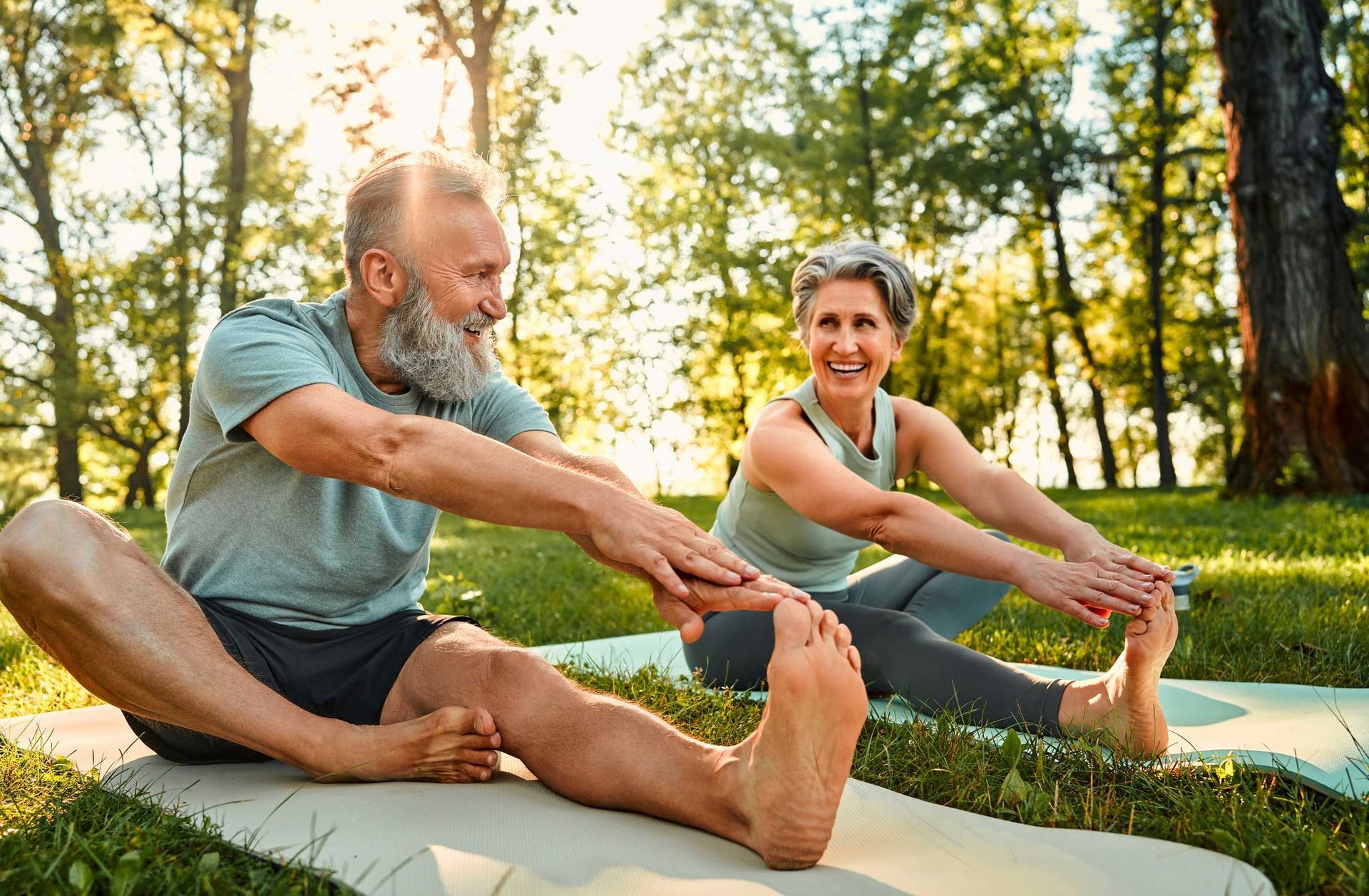 A man and a woman are stretching on yoga mats in a park.