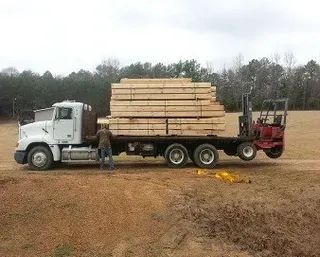 White truck carrying lumber, man standing near the flatbed. 