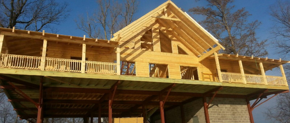 Wooden treehouse under construction, with open balconies and a pitched roof, supported by pillars.