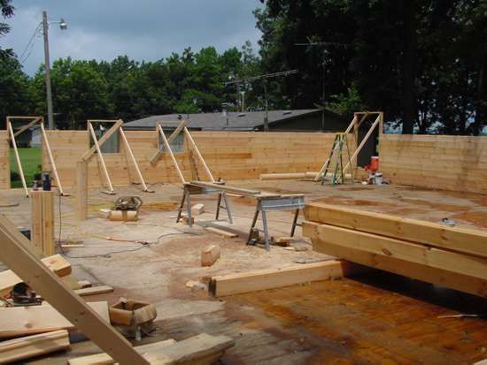 Construction site: Wood beams, partially built structure with bracing, tools, and lumber scattered about.