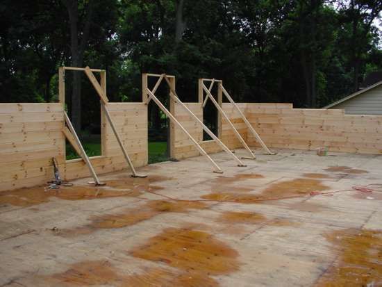 Wooden wall construction with door frames and bracing supports on a concrete slab.