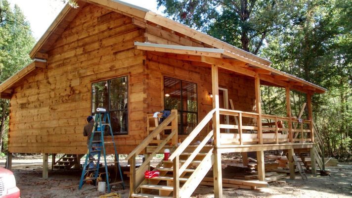 Wooden cabin under construction with porch and stairs.