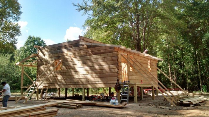 Wooden house under construction on stilts in a wooded area.