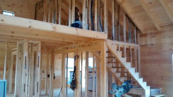 Interior of a wooden house under construction, showing a loft with stairs and framing.