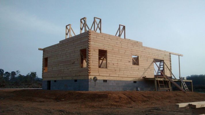 Construction of a two-story wooden building on a concrete foundation, unfinished with scaffolding and wooden supports.