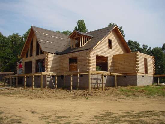 Wooden log cabin under construction, with exposed beams and unfinished roof.