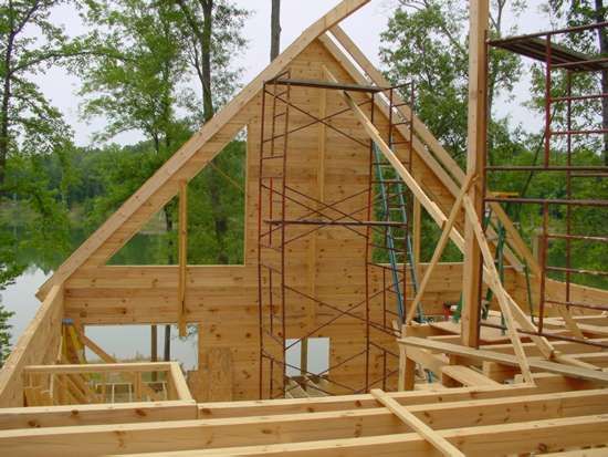 Wooden house frame under construction outdoors, scaffolding present.