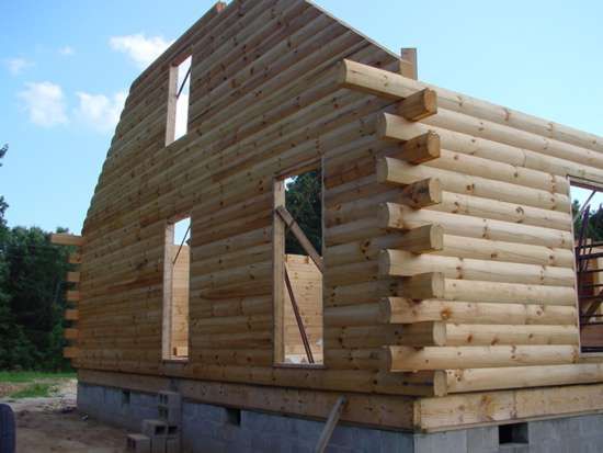 Log cabin under construction with exposed wooden logs and window openings.