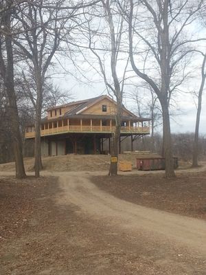 A partially built wooden house on stilts in a wooded area with a dirt road leading up to it.