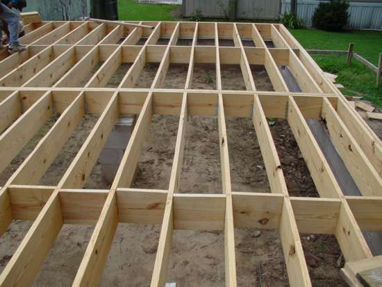 Wooden floor joists being constructed outdoors, forming a rectangular framework.