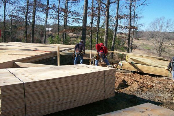 Construction workers installing wood panels on a building frame, outdoors.
