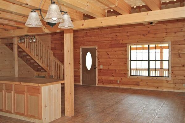 Interior of a log cabin with wooden walls, stairs, and cabinetry, door, and a multi-pane window.