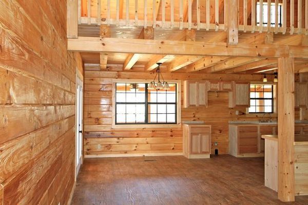 Interior of a wood cabin with a loft. Light wood walls, cabinets, and flooring. 