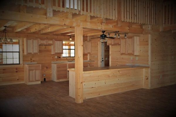 Interior of a log cabin with a kitchen, wooden bar, and loft.