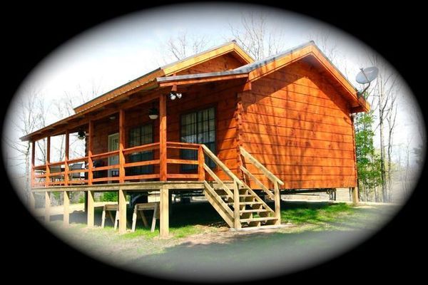 Wooden cabin with porch, railing, and stairs. Satellite dish on the roof.