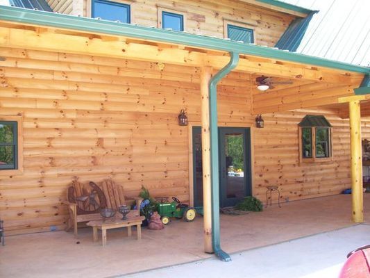 Wooden cabin exterior with porch, green gutters, and open door.