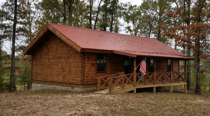 Log cabin with red roof, front porch with ramp, American flag. 
