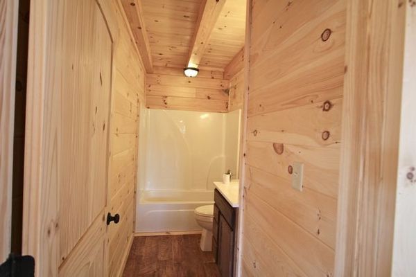 Wooden-paneled hallway leading to a bathroom with a white bathtub and vanity.