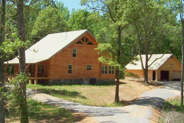 Log cabin house with detached garage on a wooded property.