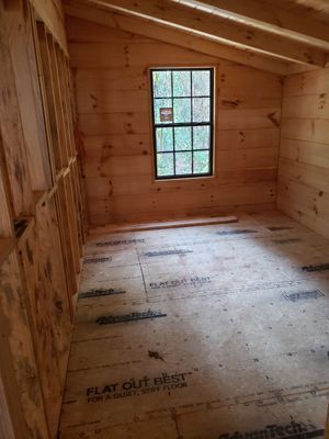 Interior of a small room under construction, with wooden walls, floor, and roof, a window, and exposed studs.