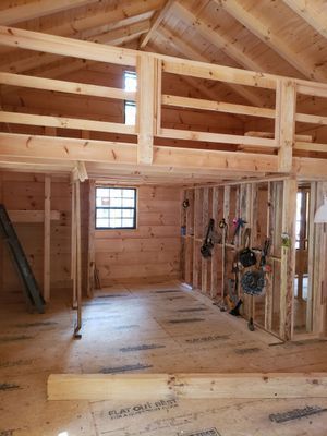 Interior view of a wooden cabin under construction with a loft area and unfinished walls.