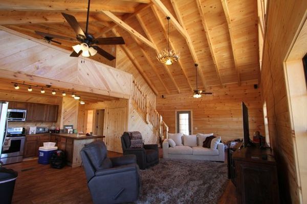Interior of a log cabin with exposed beams, furnished living area, and a kitchen.